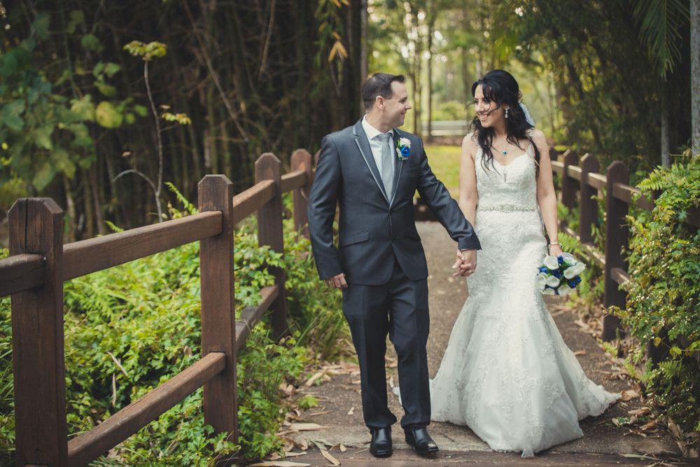 Newlyweds strolling hand in hand along wooden boardwalk surrounded by lush greenery.