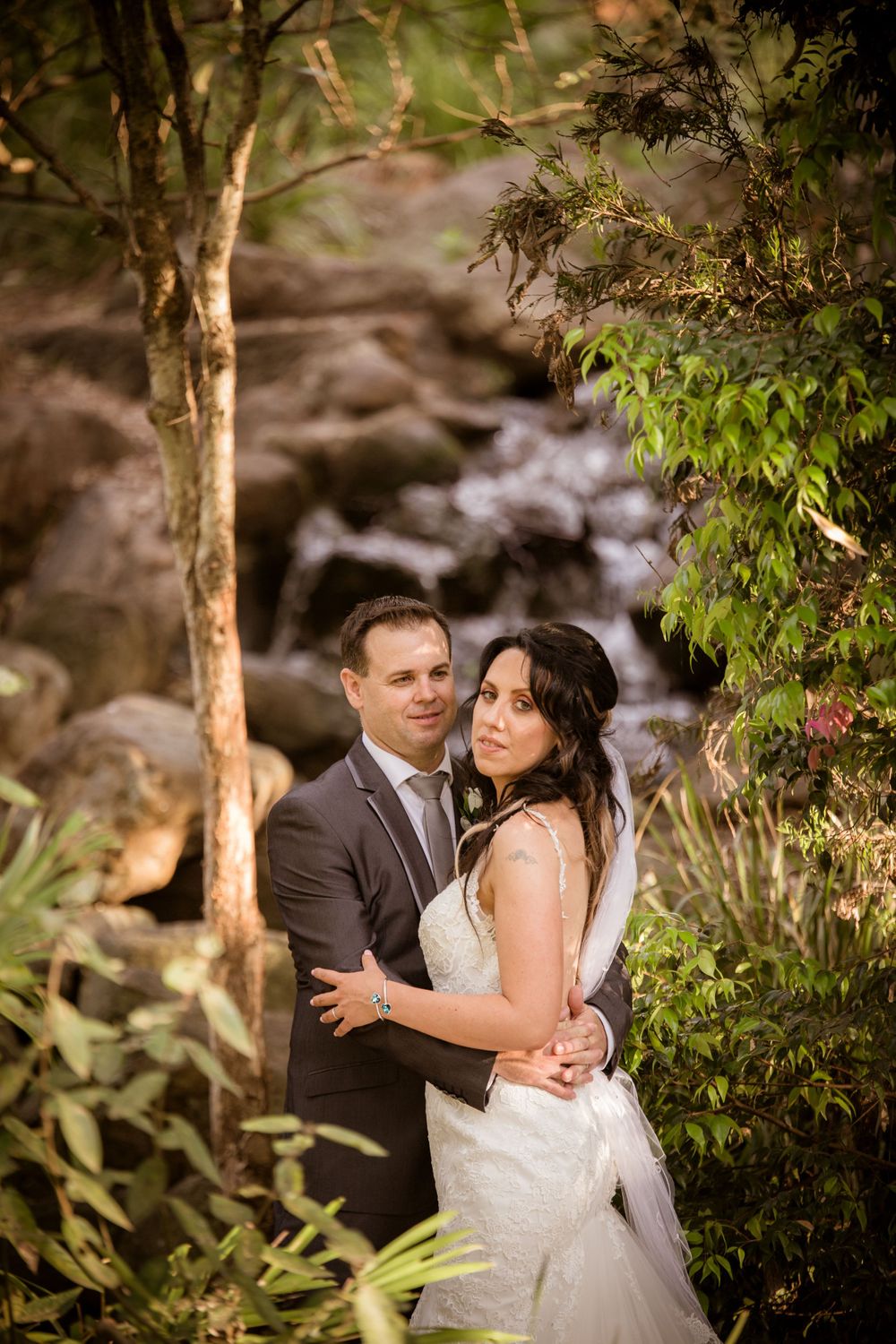 Romantic wedding portrait by a scenic creek with lush greenery and natural lighting.