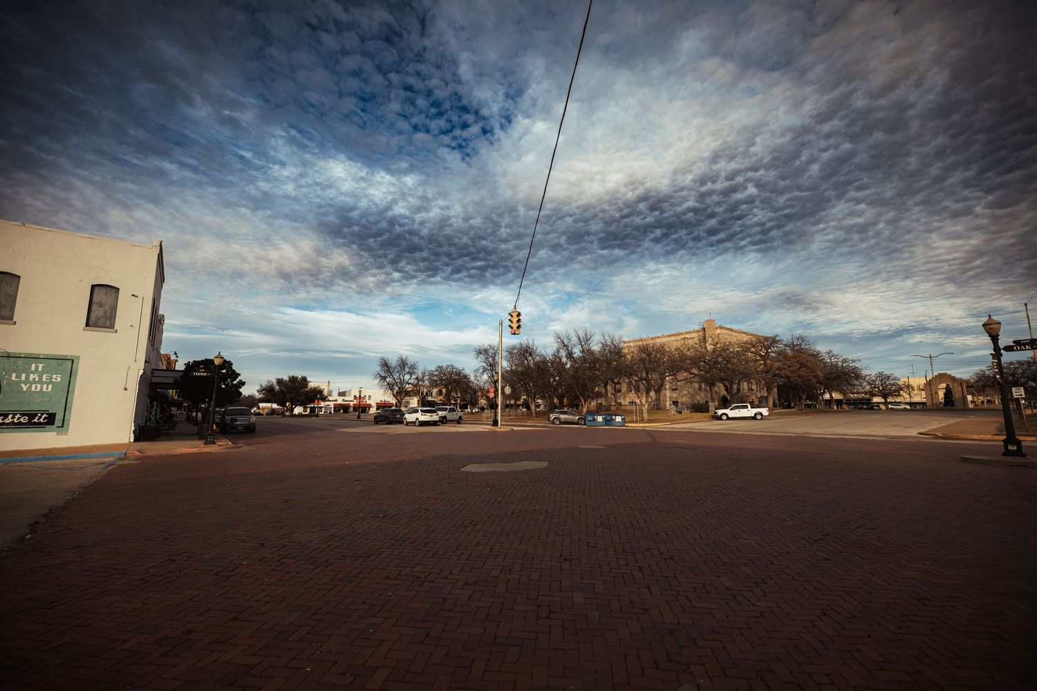 A small town intersection with vintage buildings under a dramatic cloudy sky at sunset.