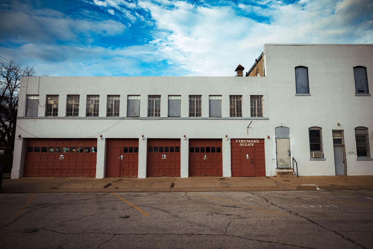 White building with five red garage doors and windows in a row on a cracked concrete surface.
