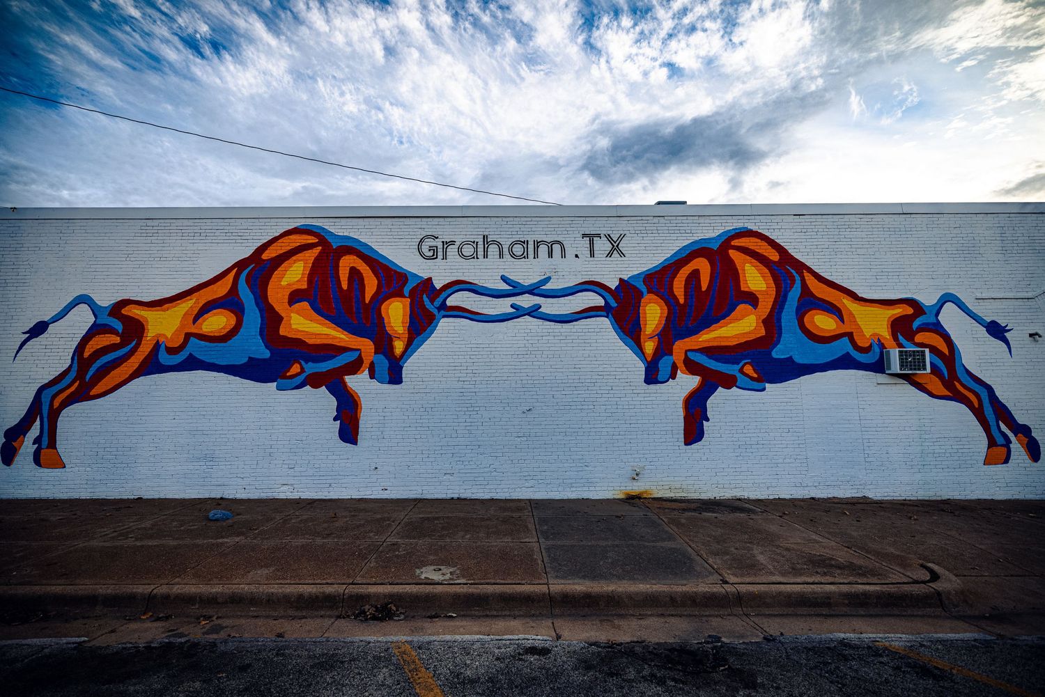 Colorful mural of two charging bulls painted in blue and orange on white wall in Graham, Texas.