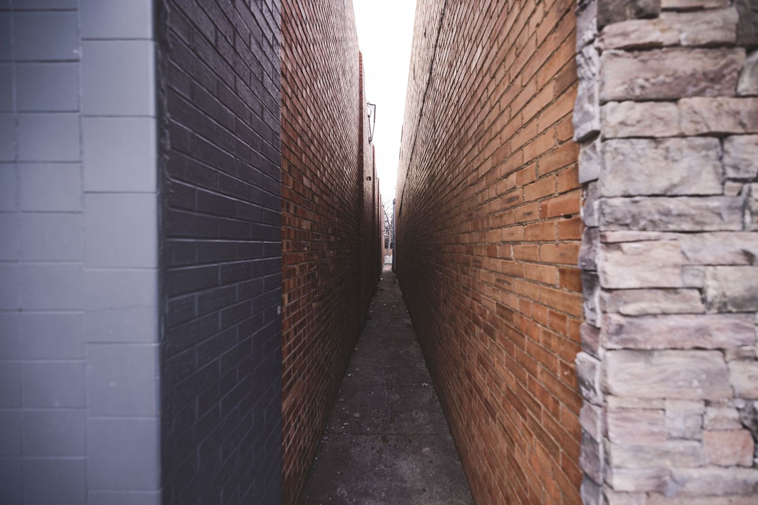 Narrow alleyway between two brick walls creating dramatic perspective and shadows.