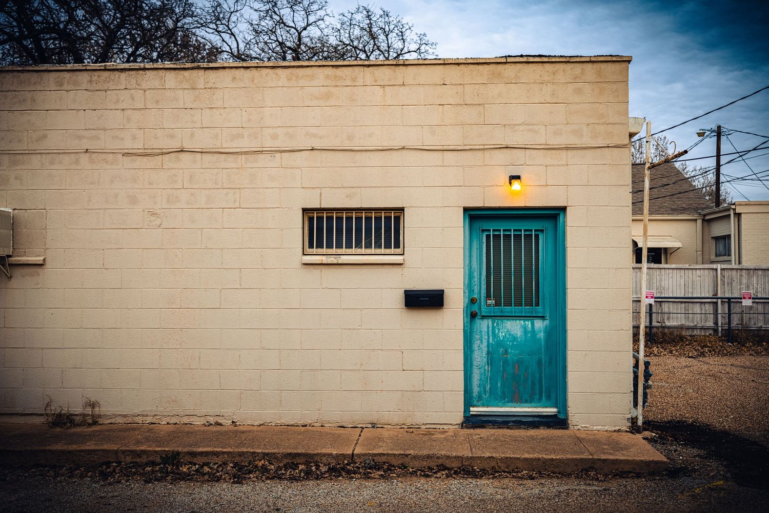 Simple white building exterior with turquoise door and barred window.