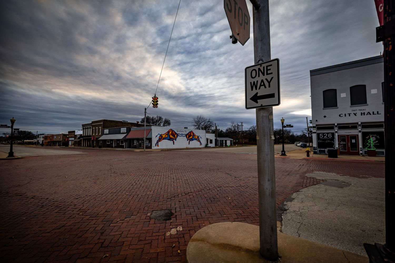 Urban street corner with brick pavement and one way sign under moody clouds.