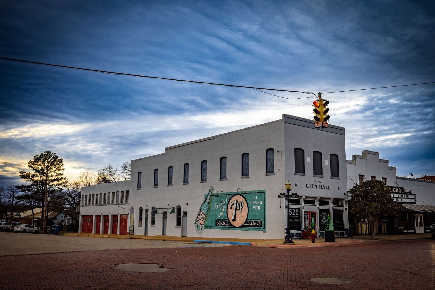 Historic white building with red doors on brick street corner under dramatic evening sky.