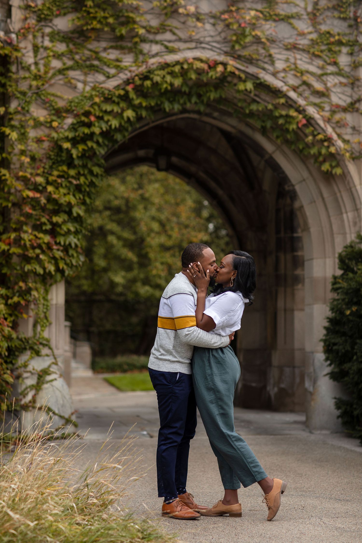 A couple sharing a romantic moment under an ivy-covered stone archway.