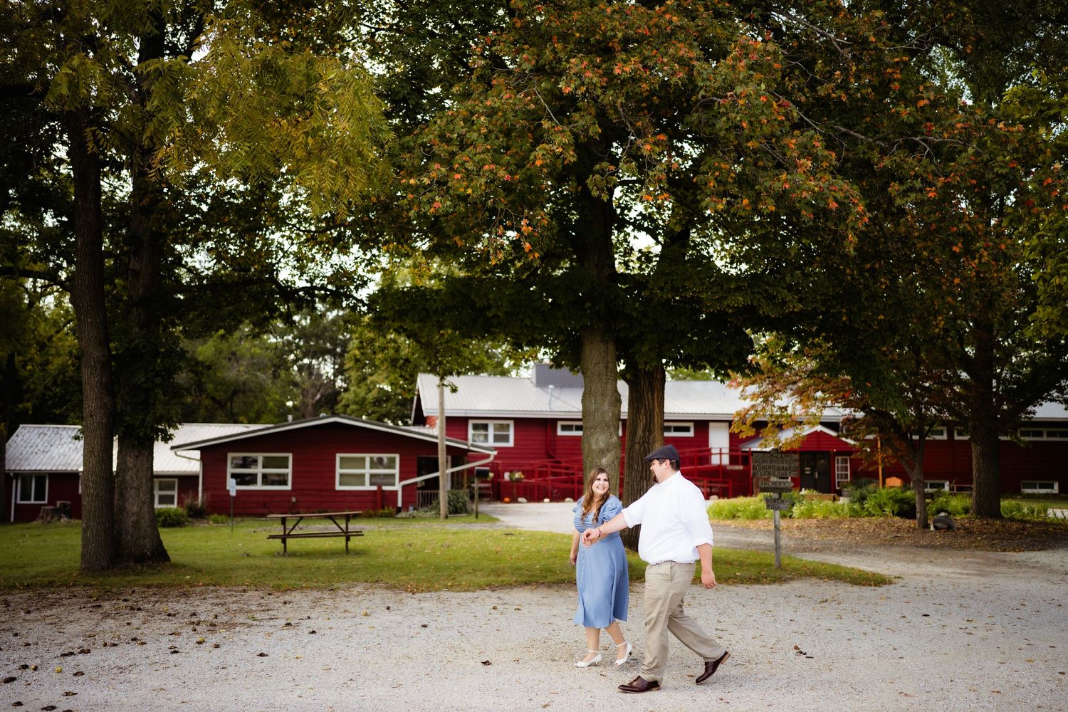 A couple strolls together near red barn buildings on a scenic autumn day.