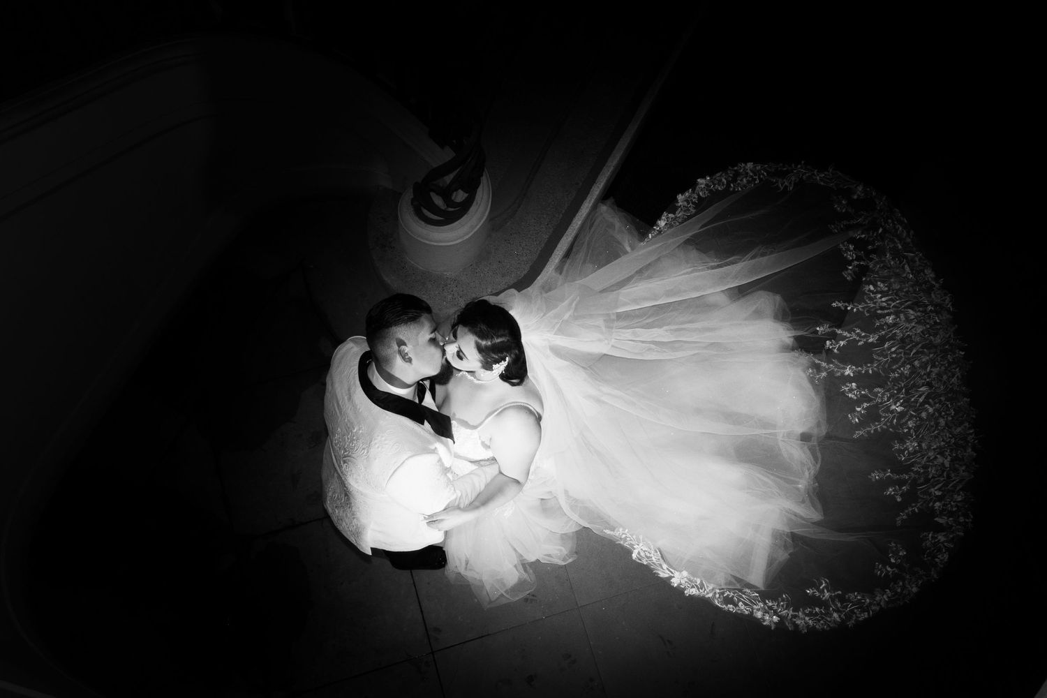 Overhead black and white photo of a couple dancing together with bride's flowing white dress creating dramatic swirl effect.