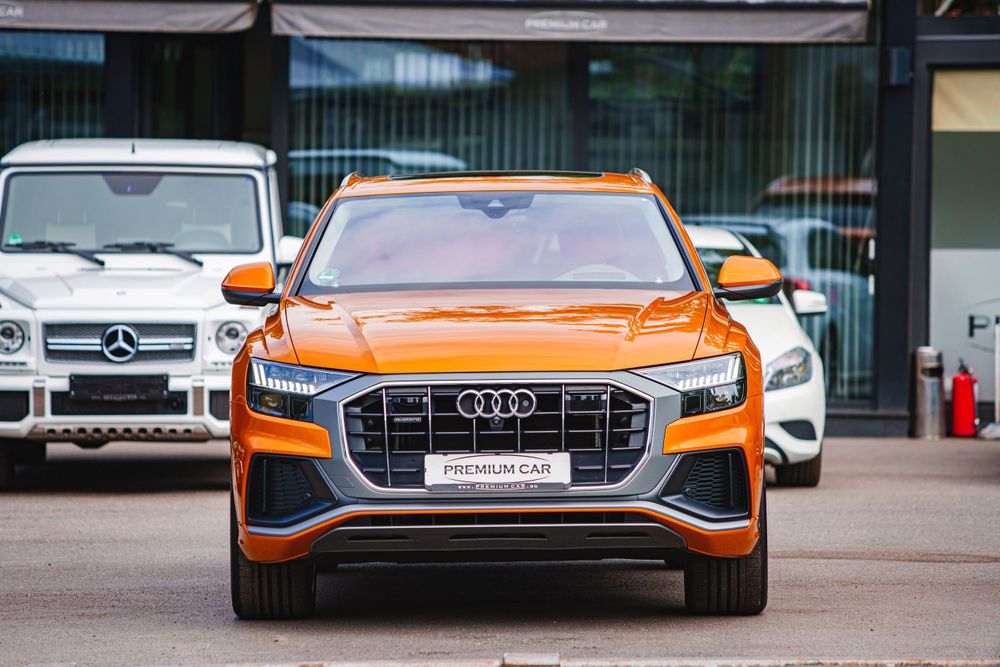 Front view of an orange Audi Q8 with distinctive octagonal grille and LED headlights.