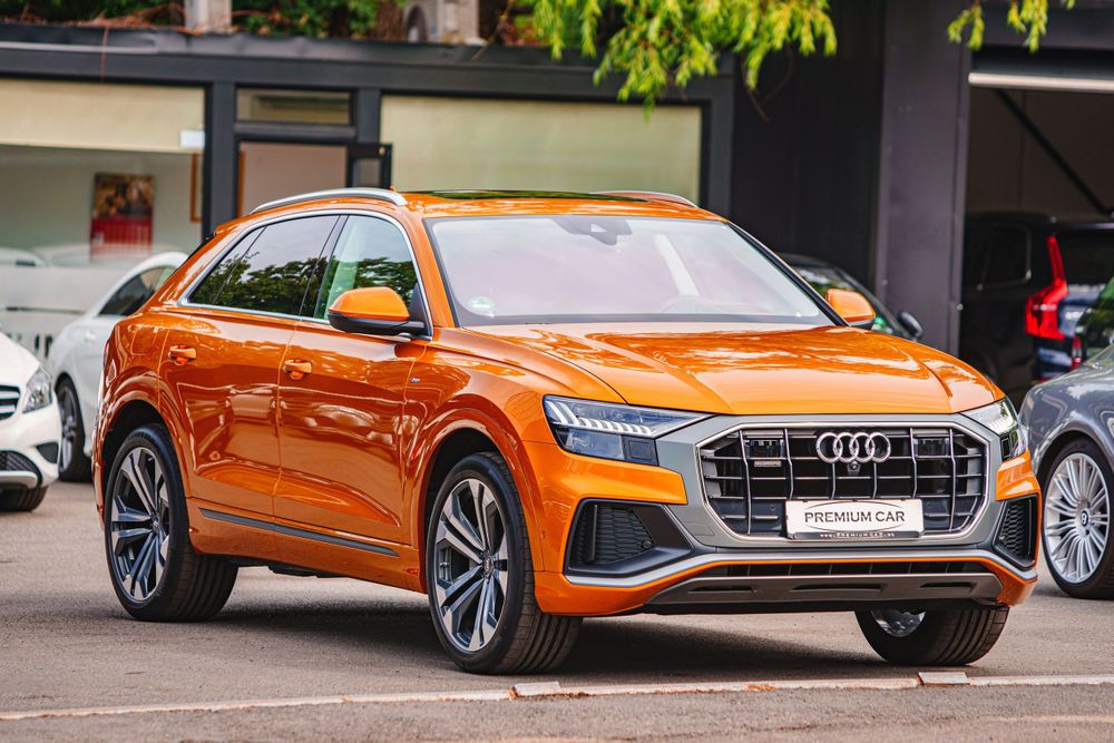 Orange Audi Q8 Sportback luxury SUV parked in front of a modern building.