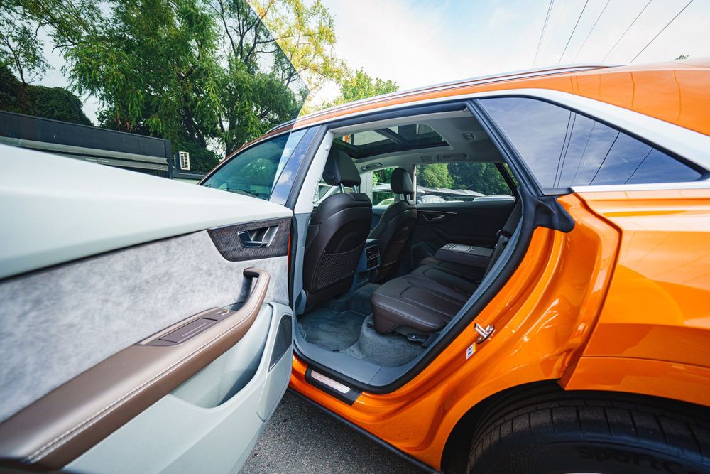 Open door view of orange Audi Q8 showing premium interior with leather seats.
