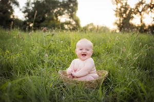 6 month old boy in a green field at sunset sitting in a basket.