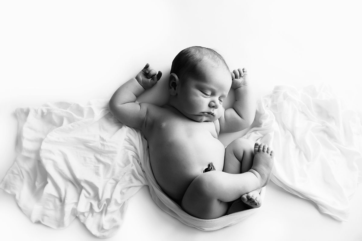Newborn baby in a white wrap curled in a womb pose.