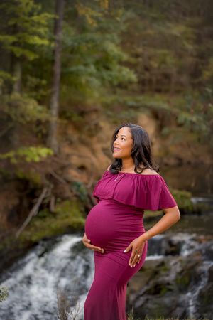 Pregnant woman in burgundy dress standing in front of waterfall at Savannah River Rapids.
