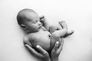 Newborn baby boy on a white blanket with his moms hands holding him.