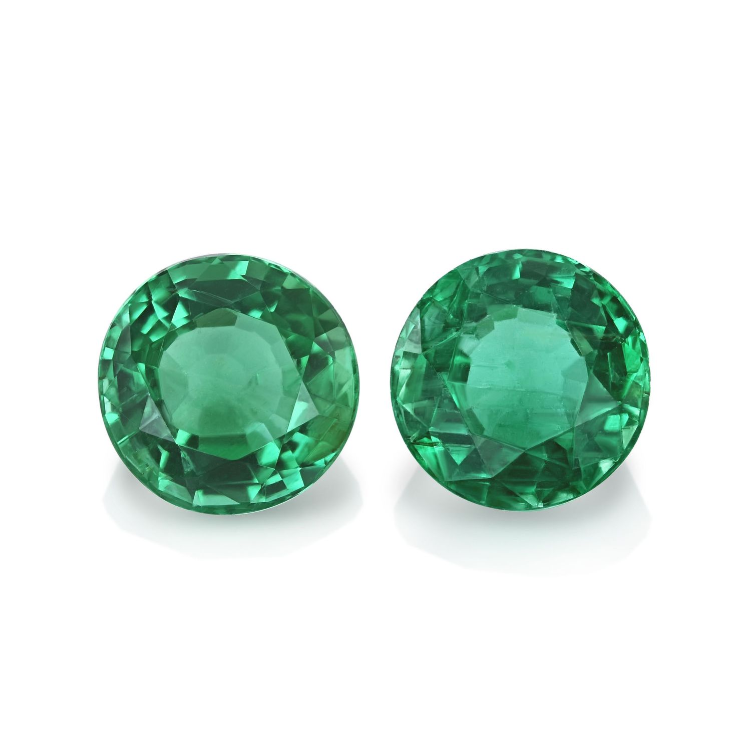Pair of round-cut emerald gemstones displaying vibrant green color.