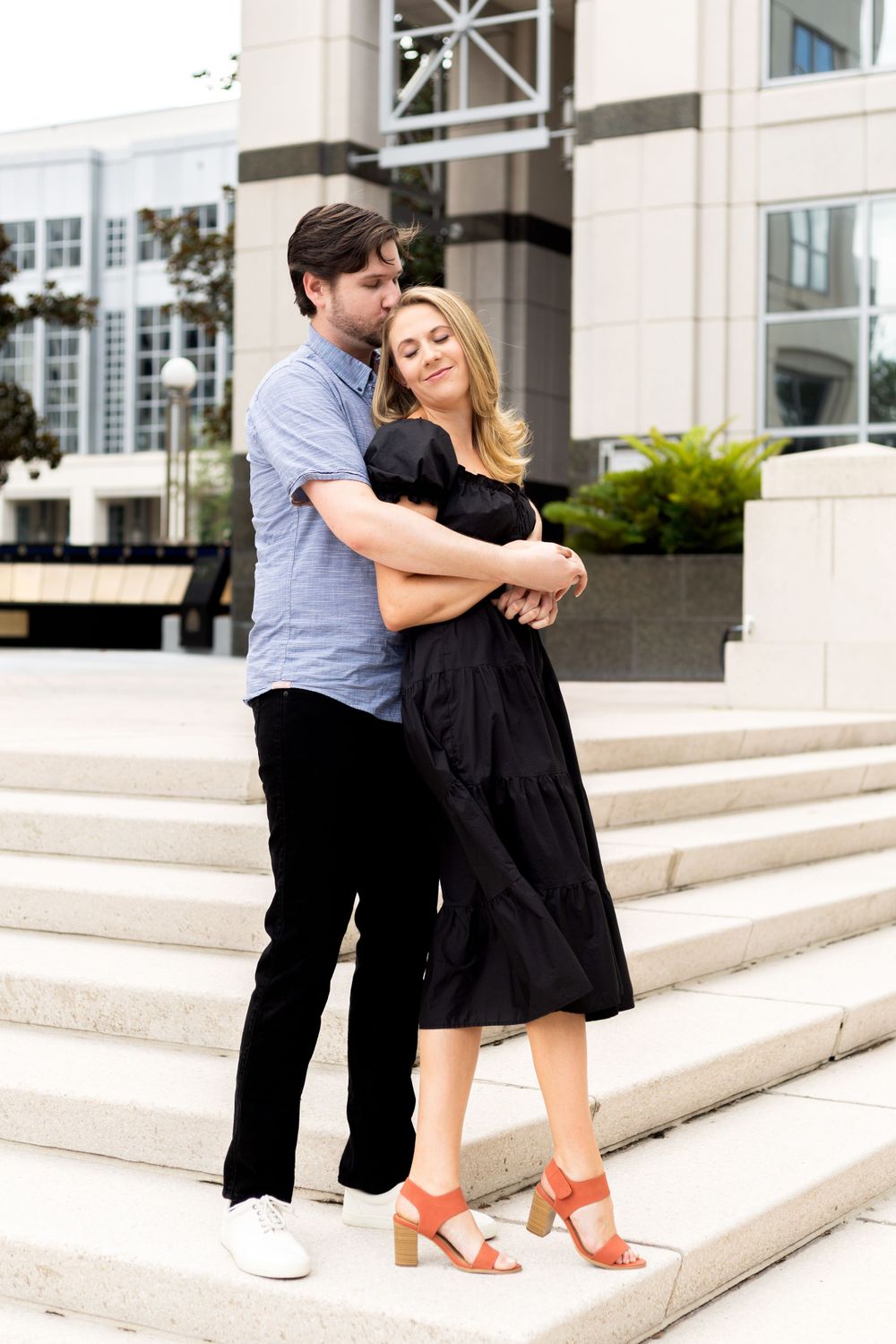 Tender embrace between couple on architectural steps with modern building backdrop.