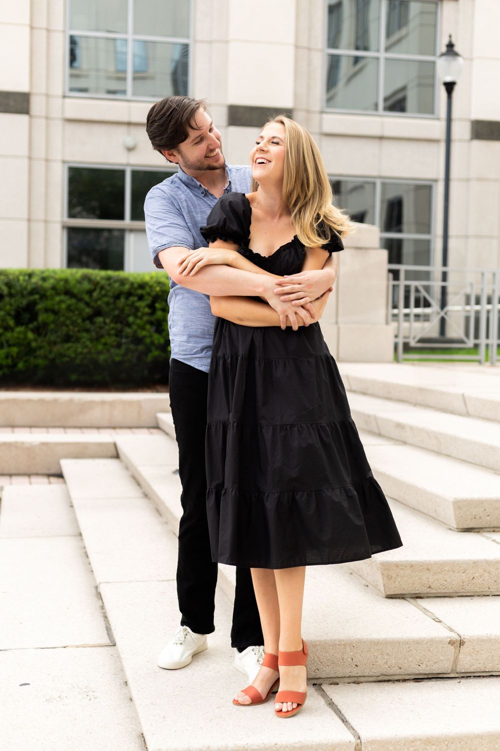 Happy couple sharing a joyful moment while embracing on outdoor steps of an urban building.