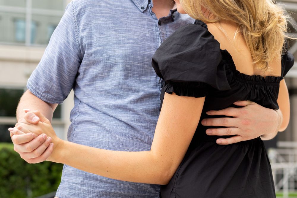 Close-up of couple dancing together, wearing coordinated casual outfits against urban backdrop.