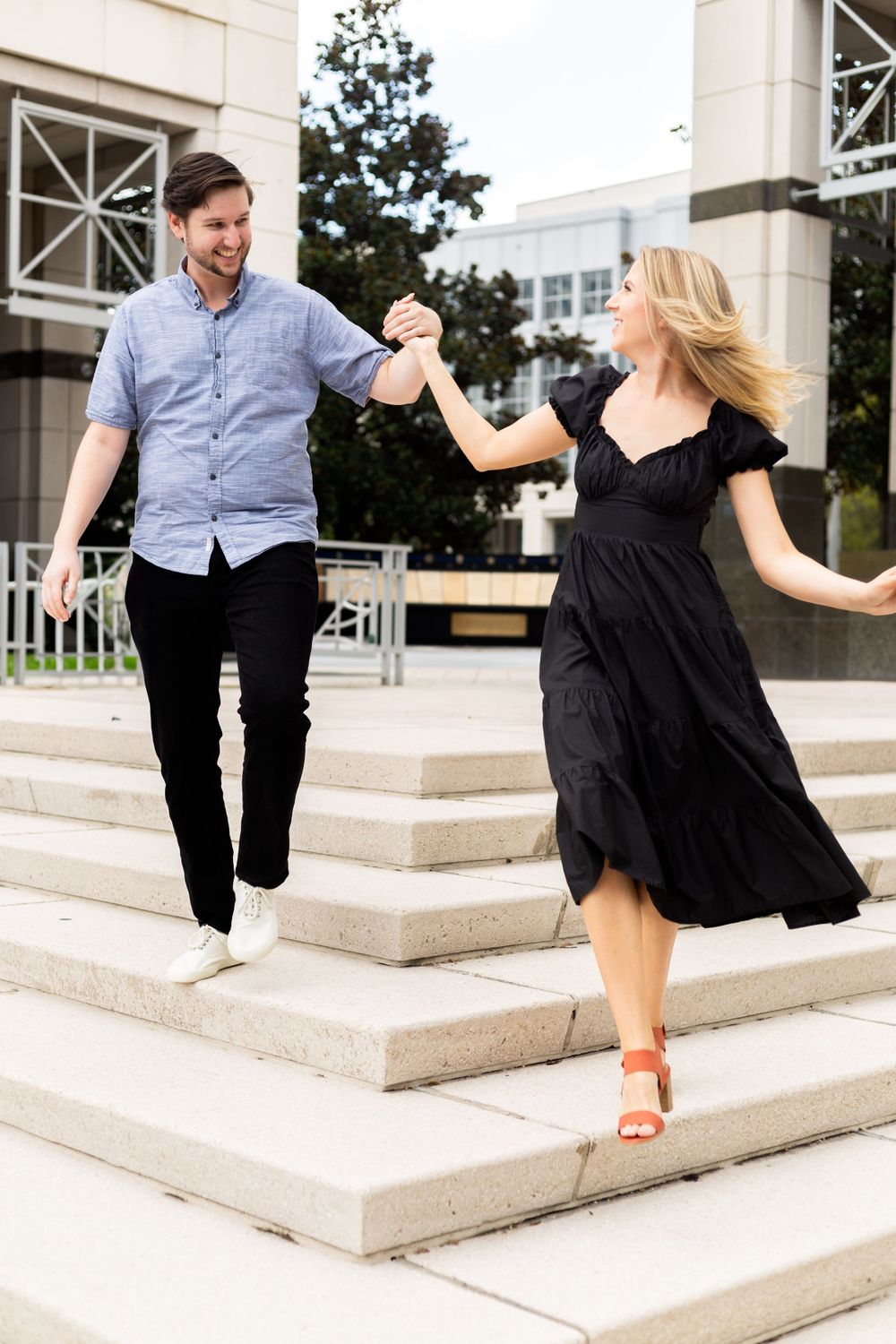 Dancing couple on stone steps, her black dress flowing as they move together outdoors.