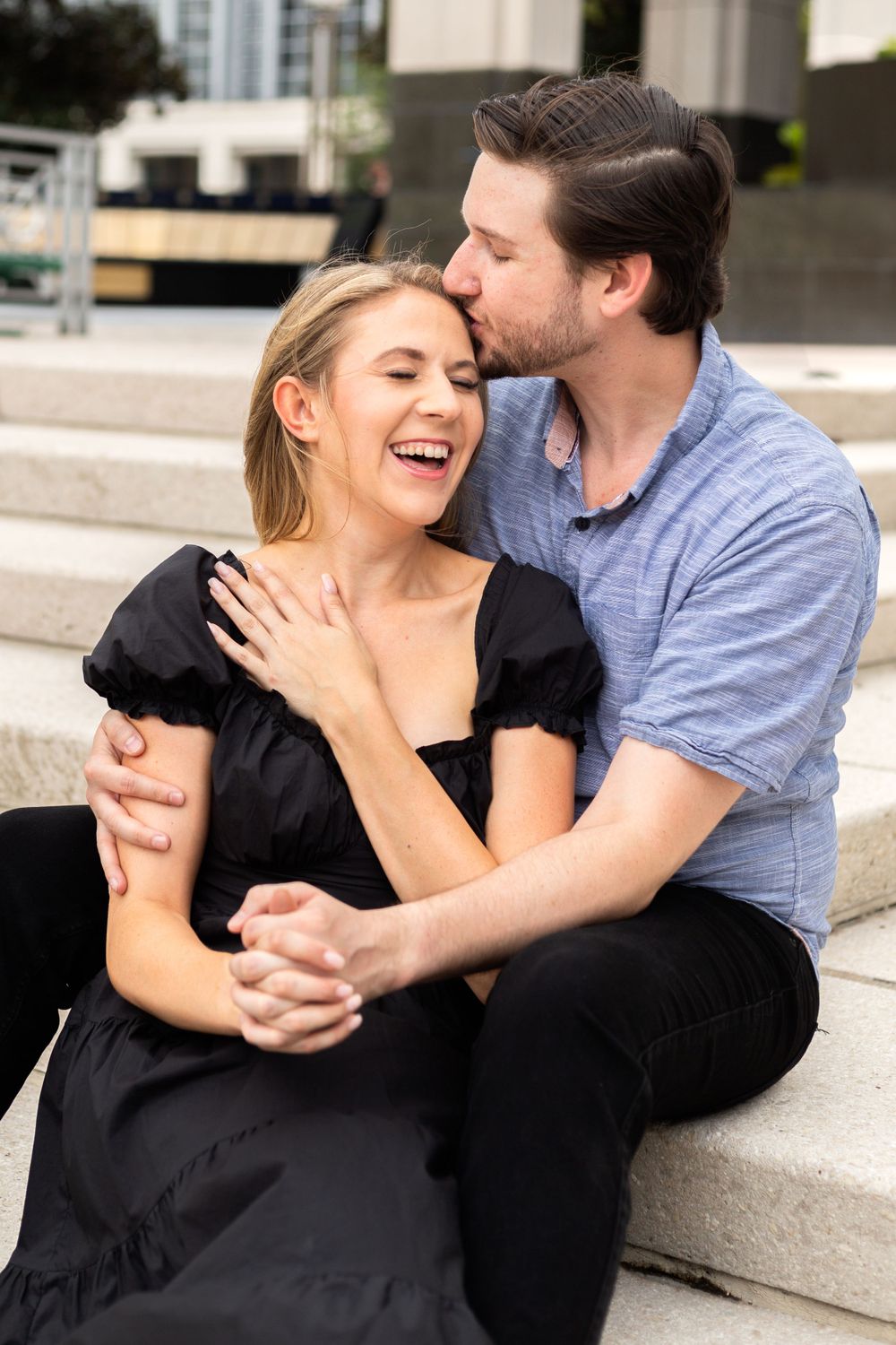Candid moment of laughter and affection shared between couple seated on stone steps.
