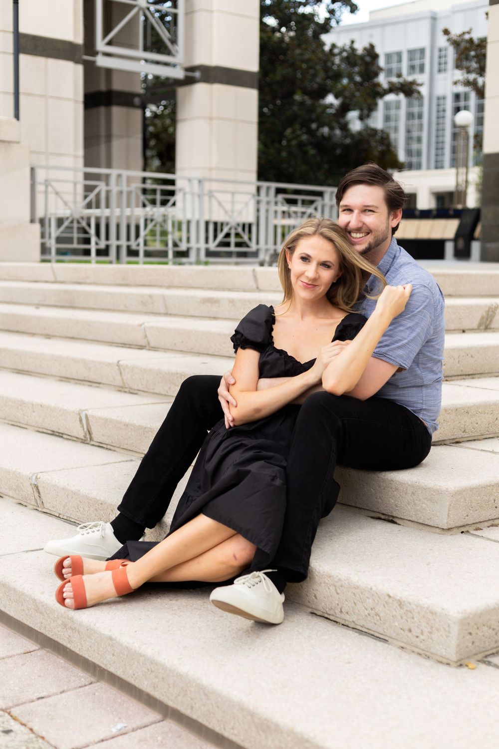 Couple relaxing together on stone steps outside modern building in coordinated outfits.