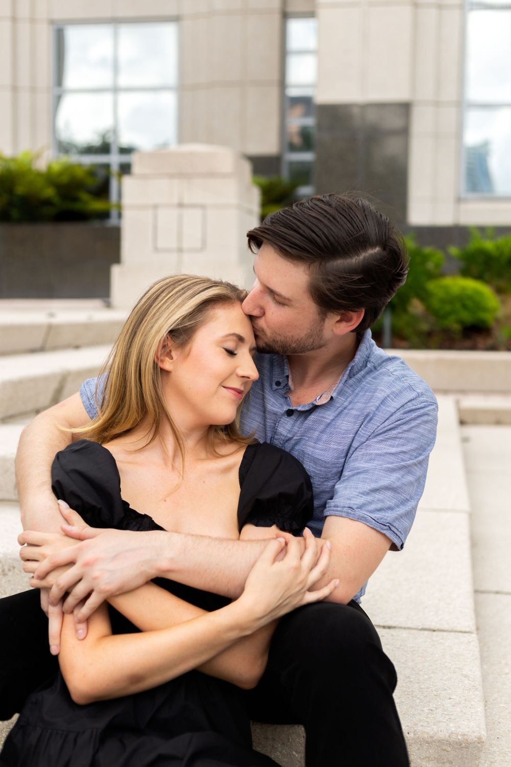 Intimate embrace shared between couple on outdoor steps with modern architecture backdrop.