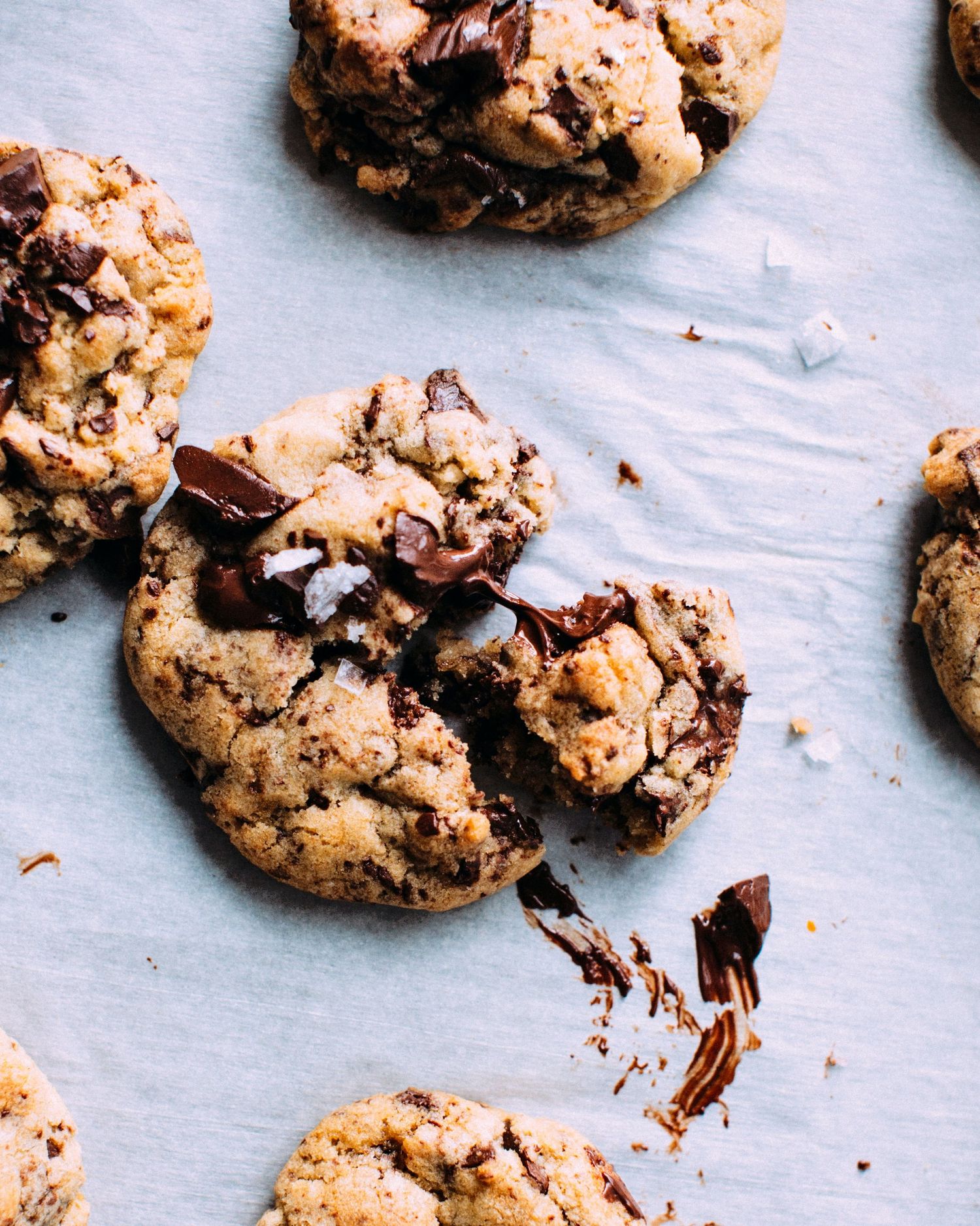 Close-up of gooey chocolate chip cookie with melted chocolate chunks on parchment paper.