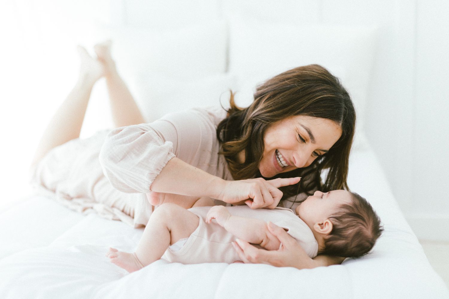 Parent and baby share tender cuddle moment on white bedding.