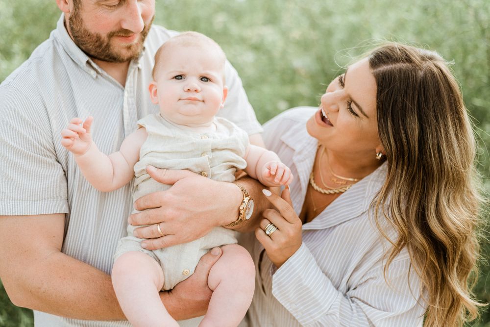 A family shares an intimate moment outdoors while holding their baby in casual attire.