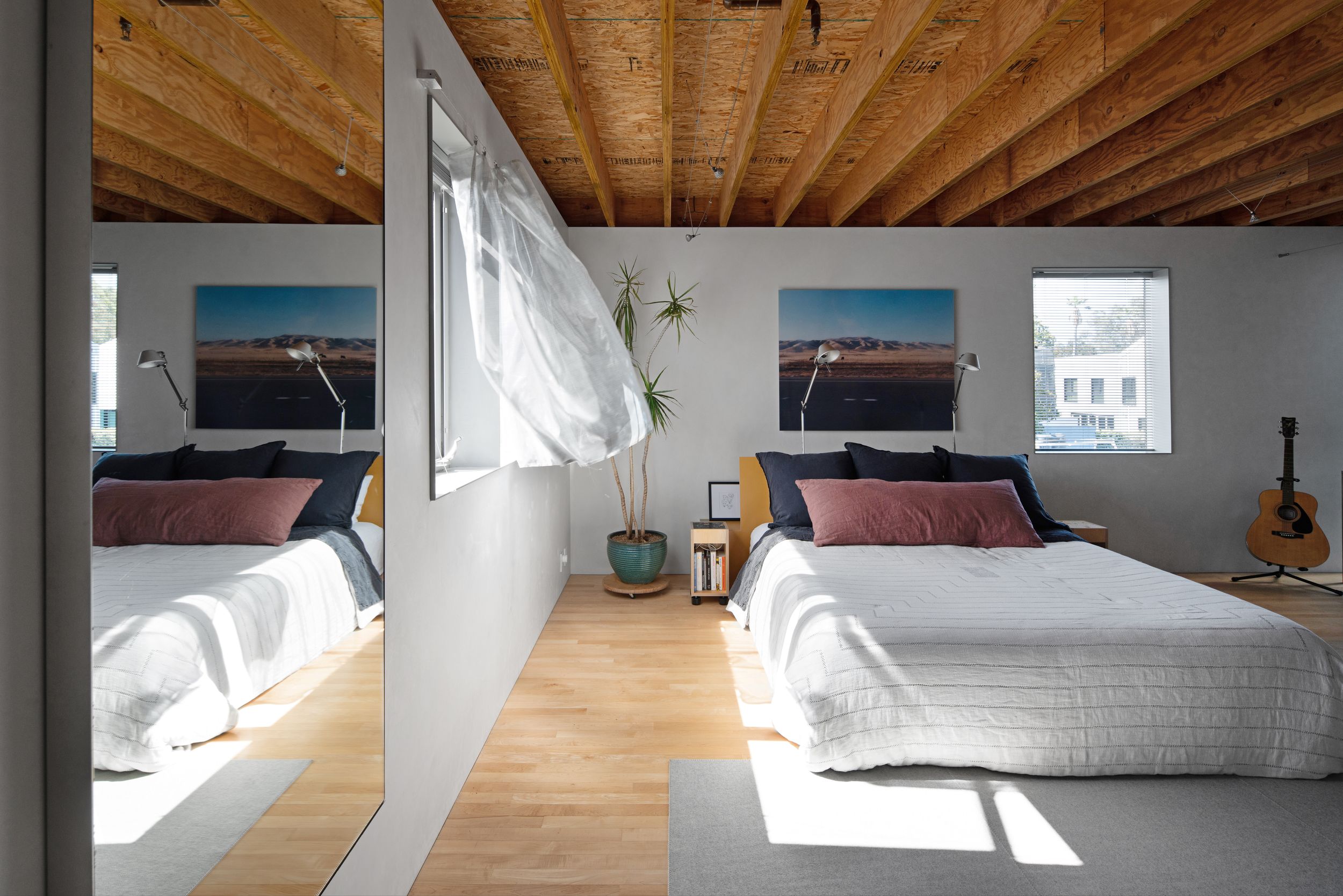 Bright bedroom with exposed wooden beams, white bedding, and large windows letting in natural light.