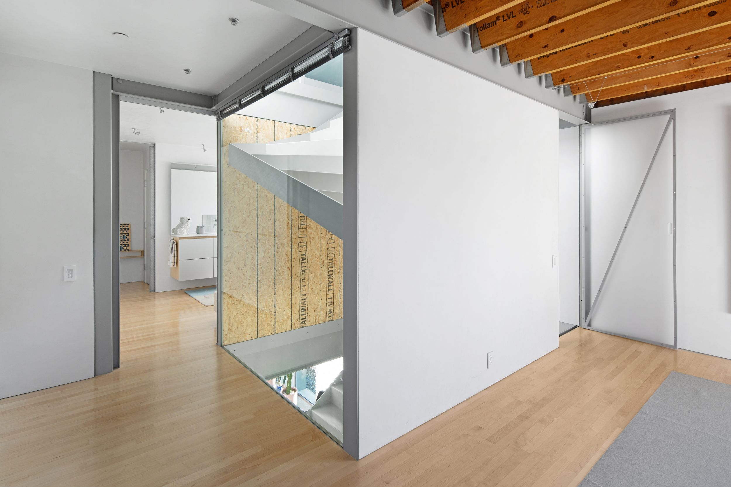 Modern hallway with wooden floor and mirrored wall detail showing architectural elements.
