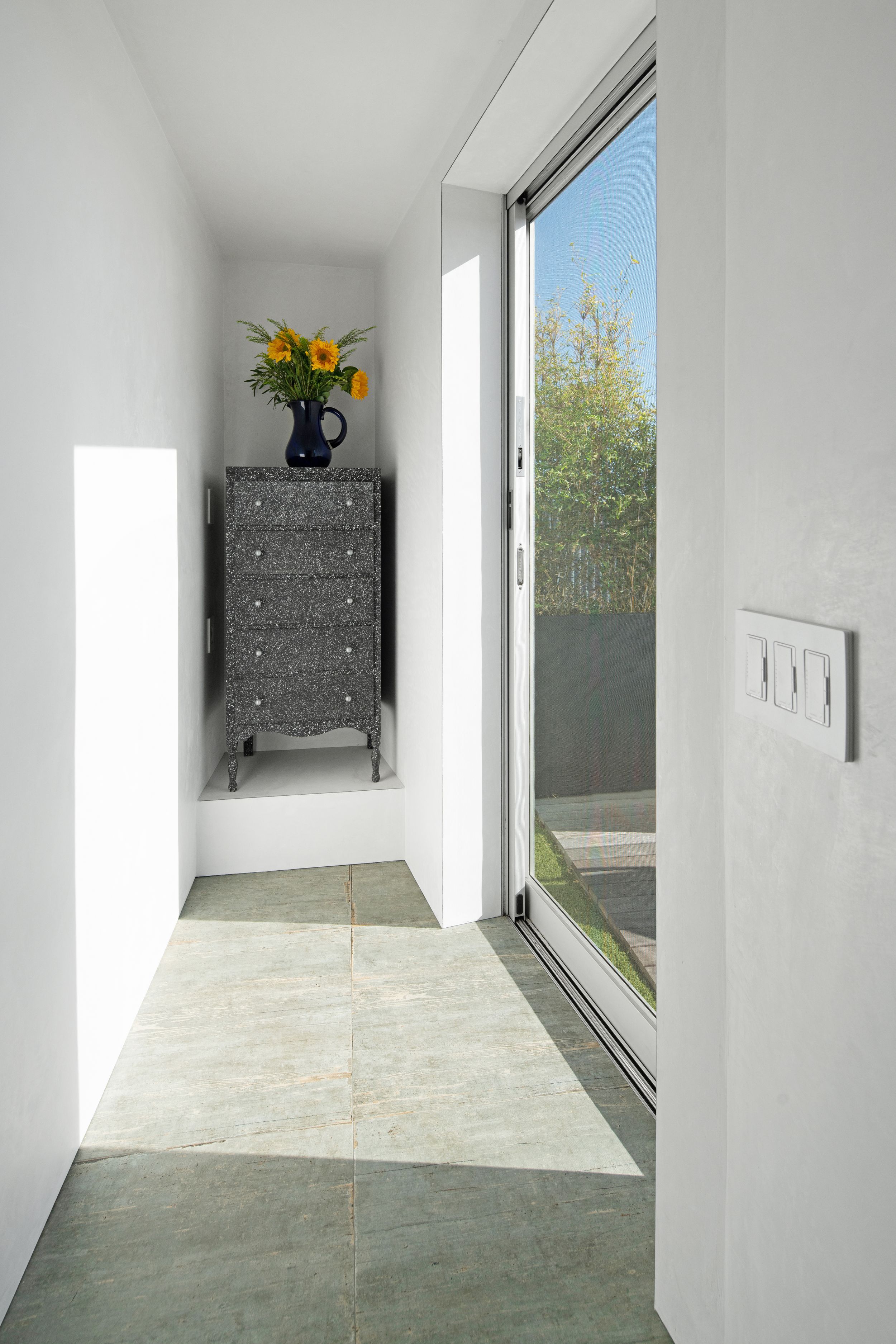 Narrow entryway with grey dresser, yellow flowers, and floor-to-ceiling window.