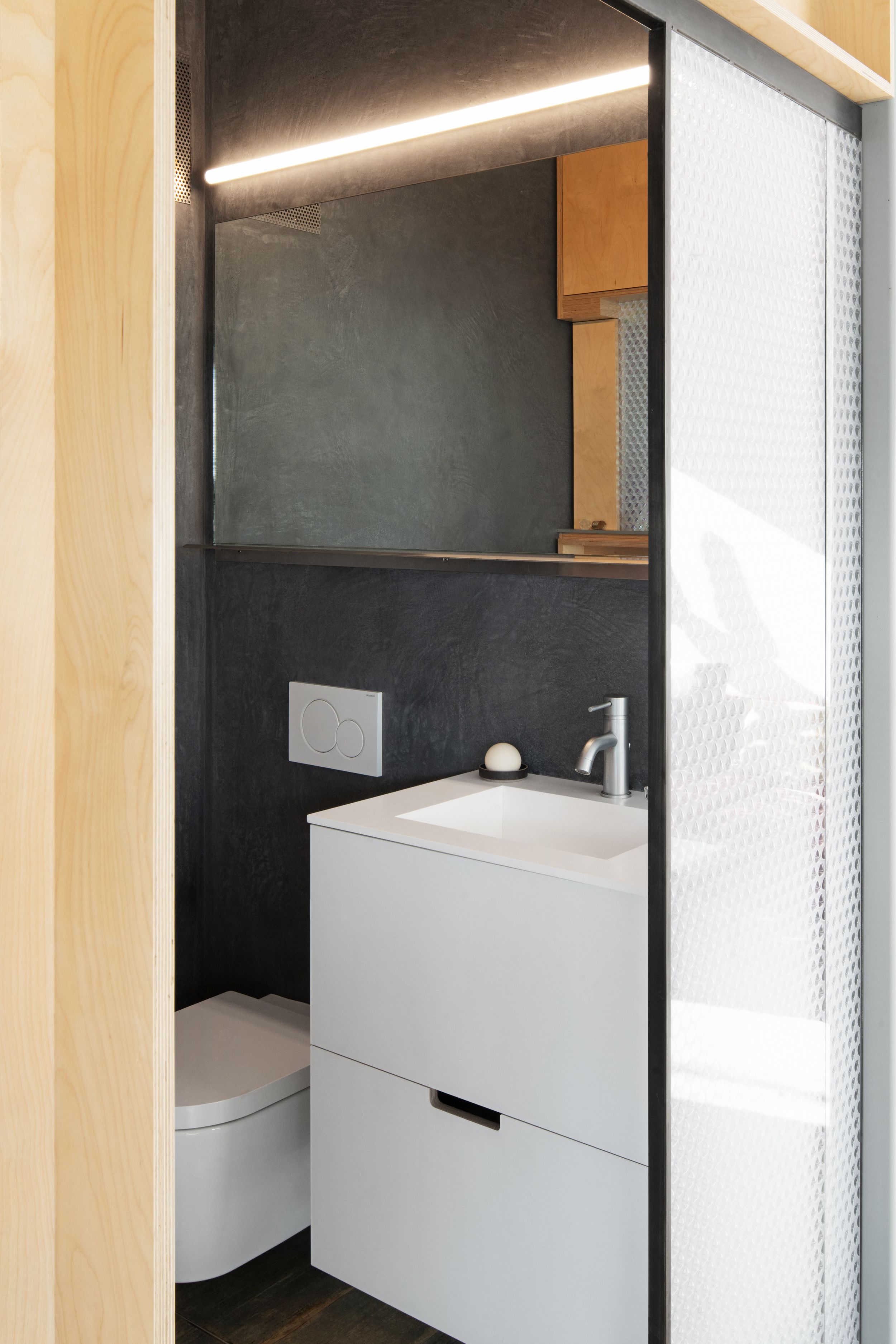 Modern minimalist bathroom with white vanity unit and black wall tiles featuring clean lines and LED lighting.