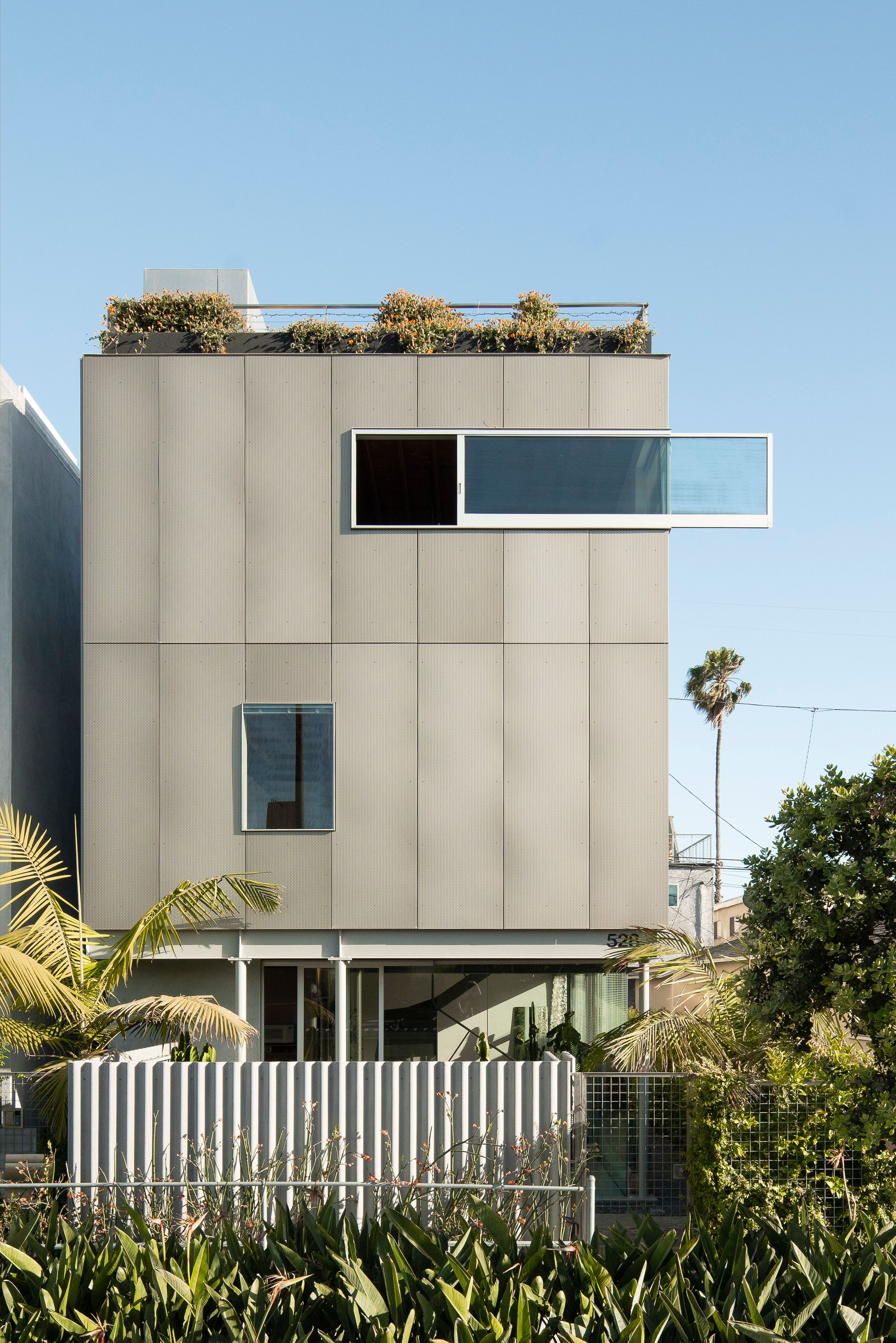 Modern cubic house exterior with grey paneling and a rooftop garden featuring horizontal window design.