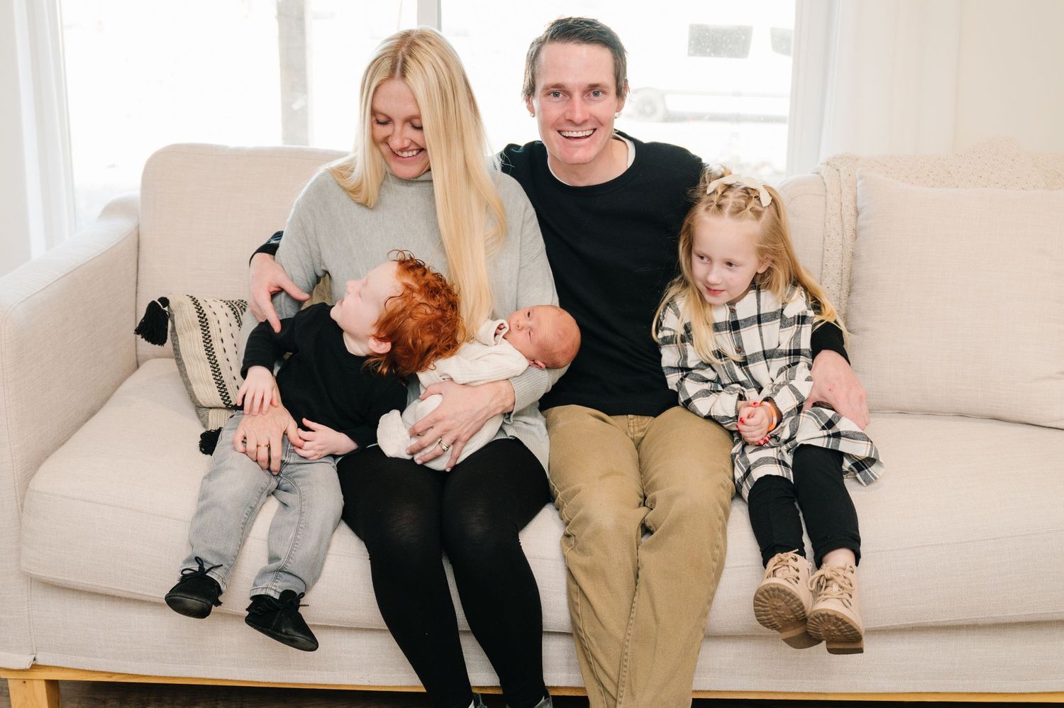 Family sitting together on white couch with small dog and baby.