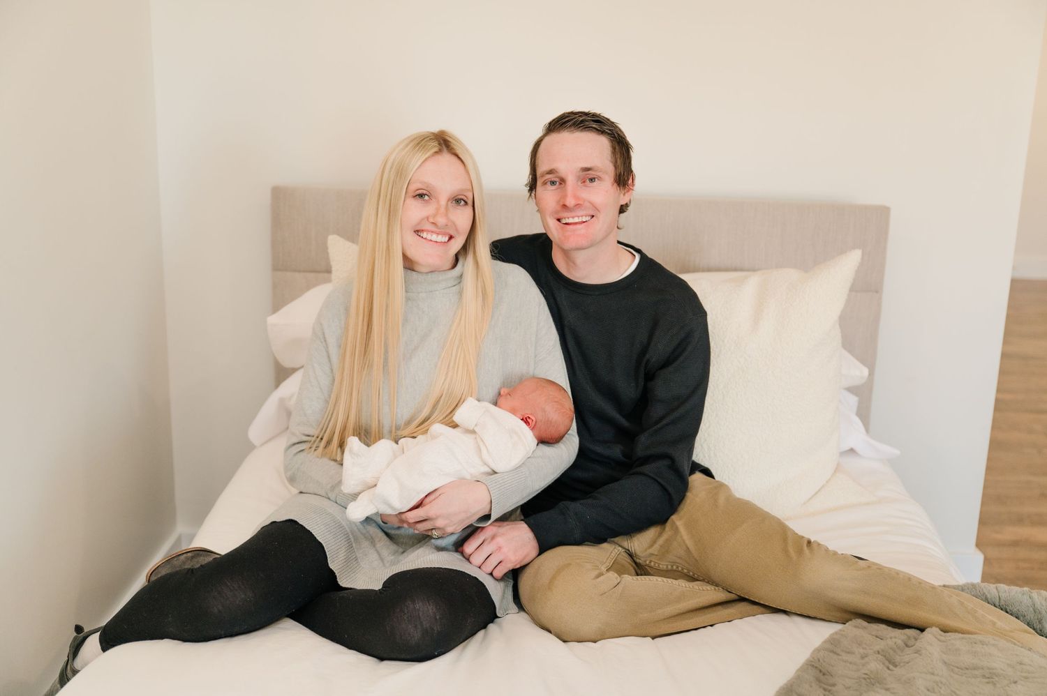 Family of three relaxing on bed with newborn baby.