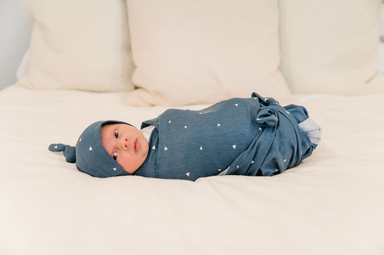 Newborn baby wrapped in blue polka dot swaddle lying on white couch.