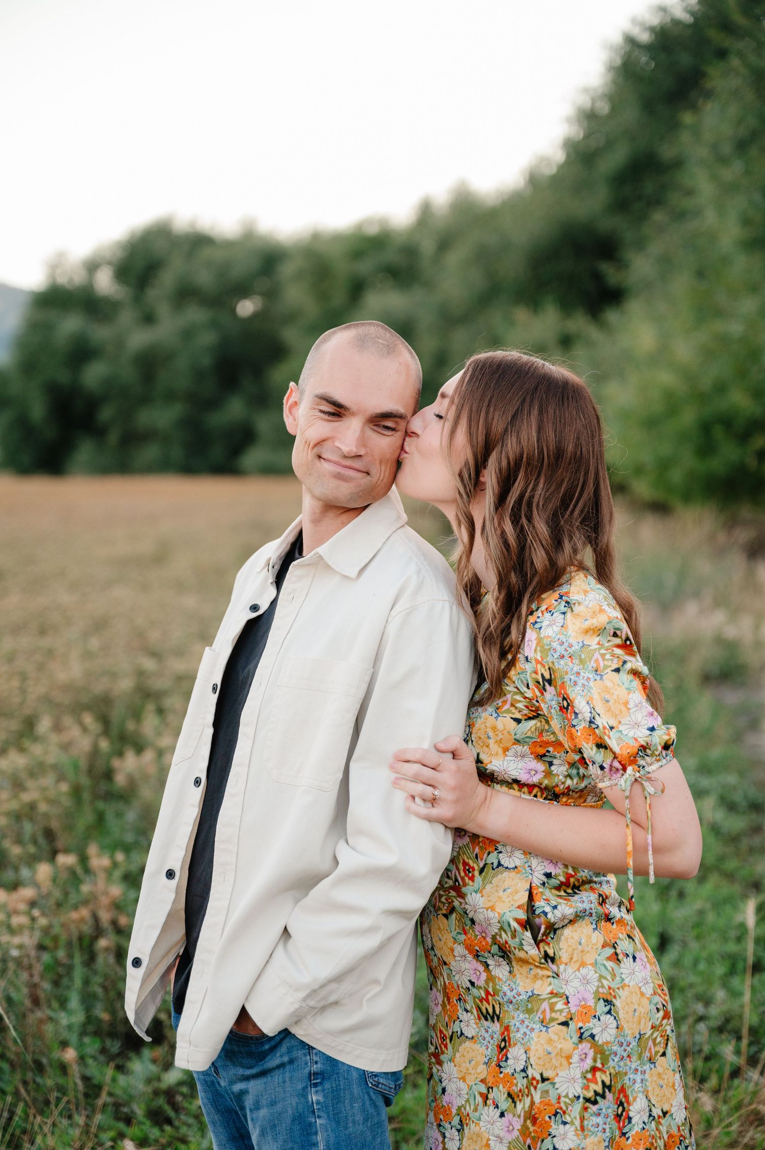Romantic couple's portrait in a summer field with floral dress and light jacket.