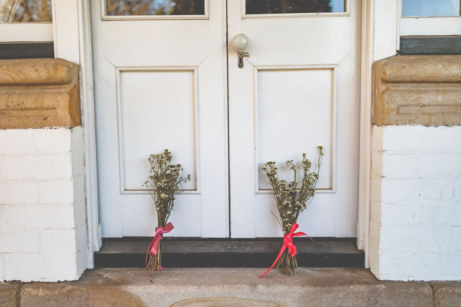 Two white doors with small floral bouquets tied with red ribbons at their base.