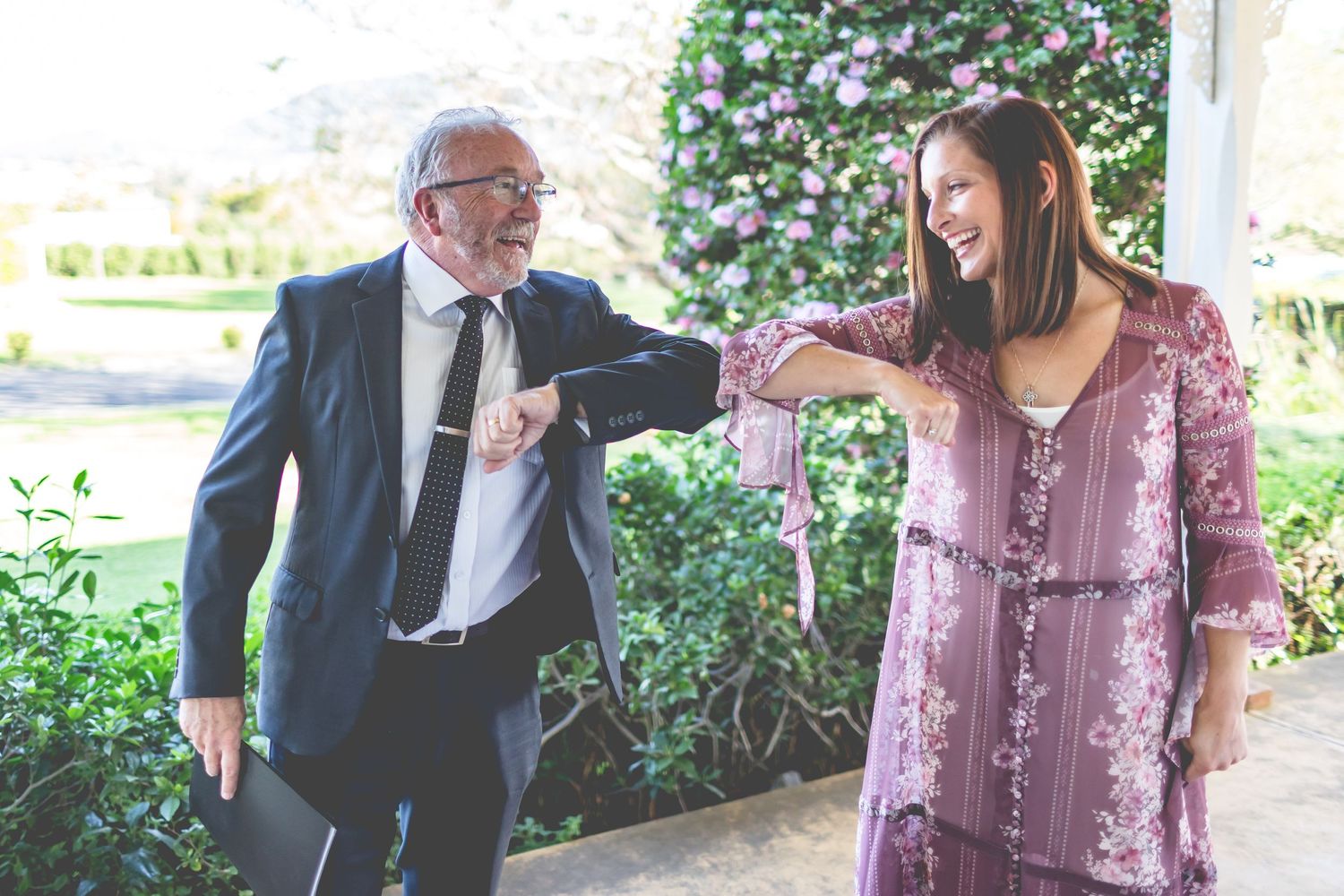Pair sharing a joyful moment while performing elbow bump greeting outdoors.