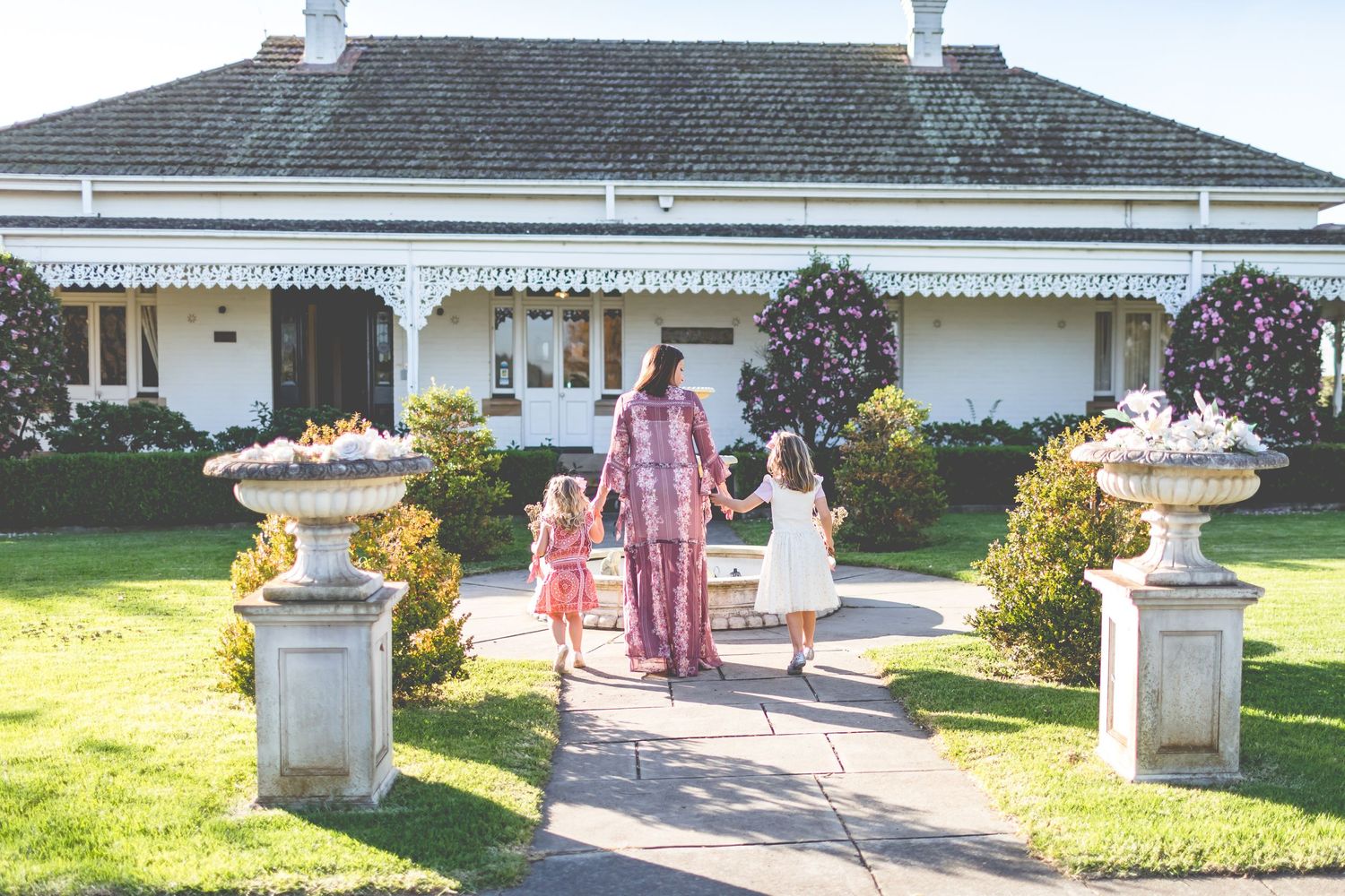 Family walking along path towards white house with manicured garden.