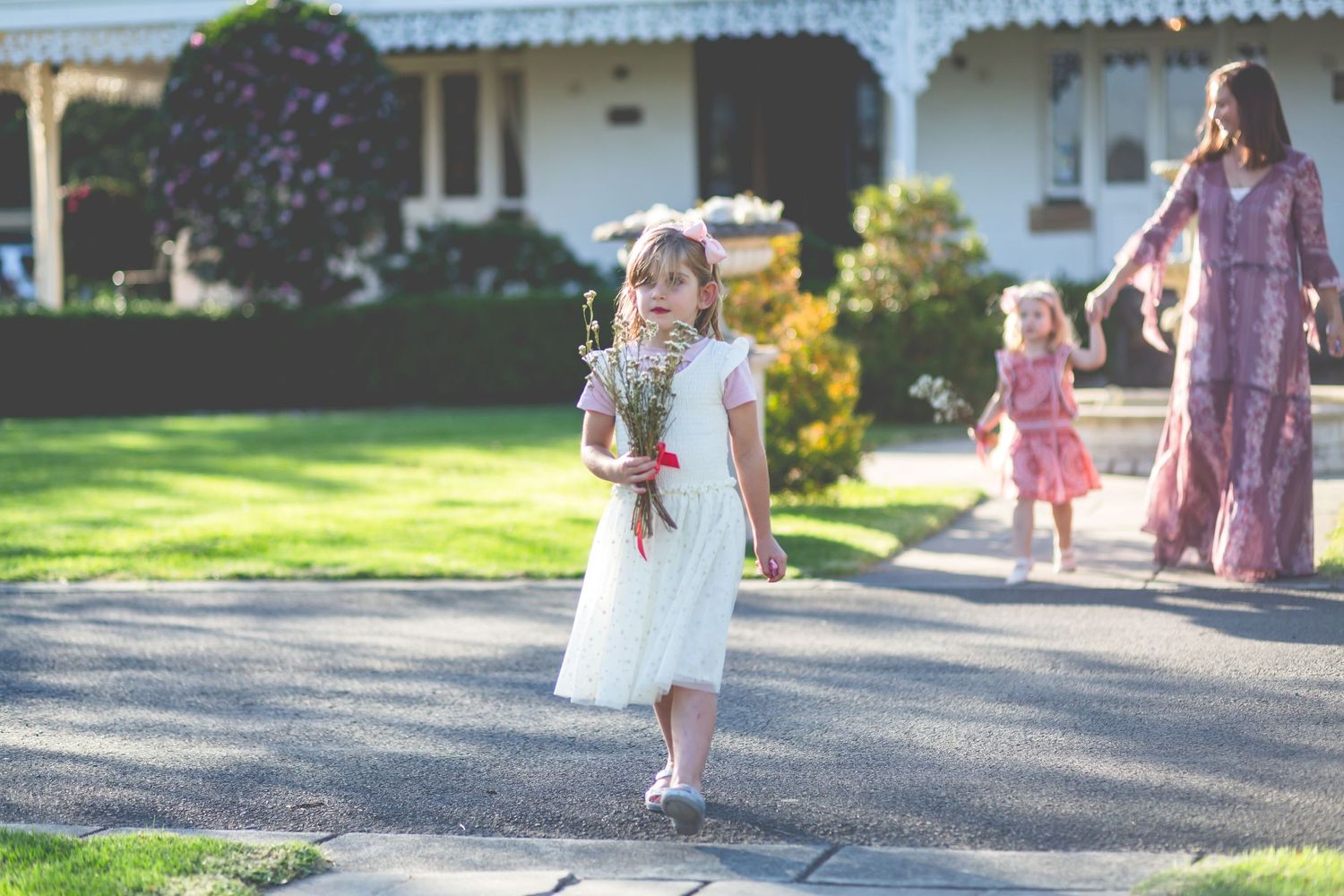 Children walking on garden path carrying flowers with house in background.
