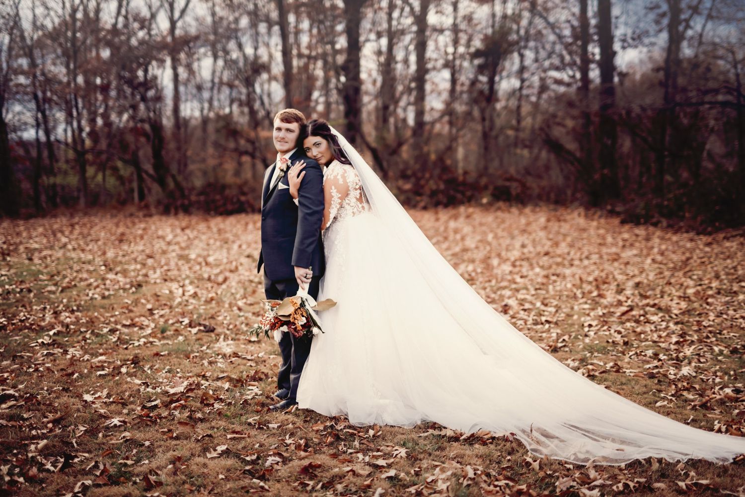 Bride in flowing white dress walking through autumn leaves during fall photo shoot.
