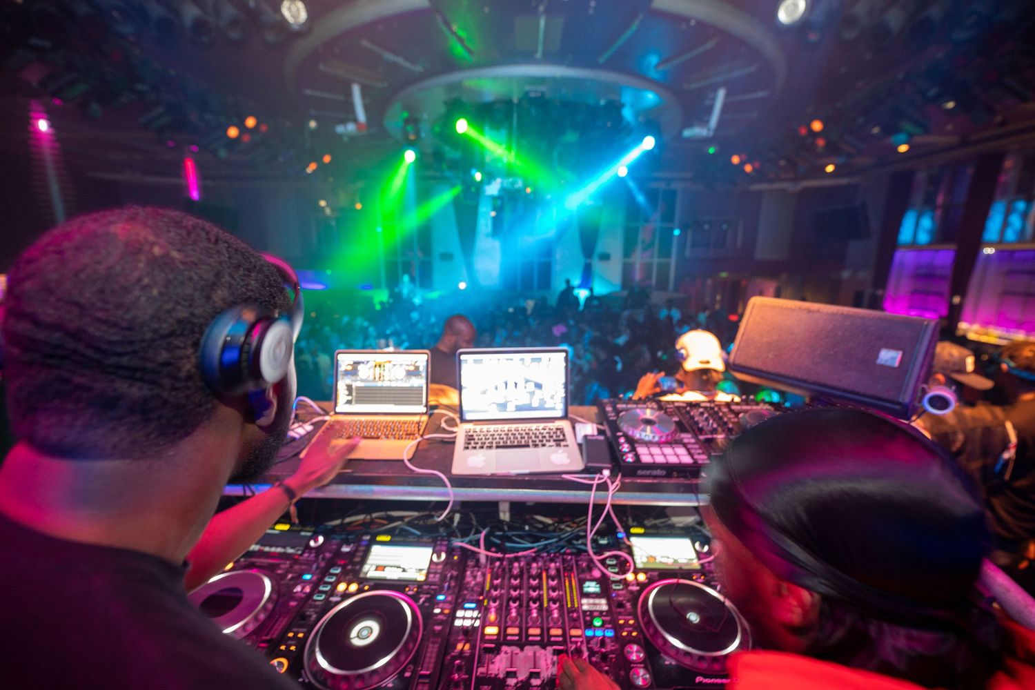 DJ performing at a vibrant nightclub with colorful green and purple stage lights illuminating the crowd.