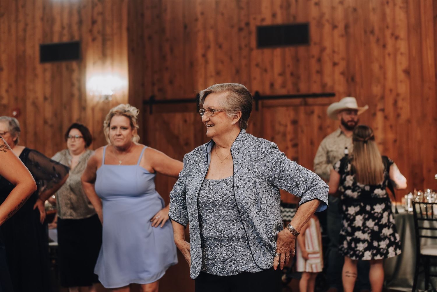Wedding guests dance and celebrate in a rustic wood-paneled reception venue.