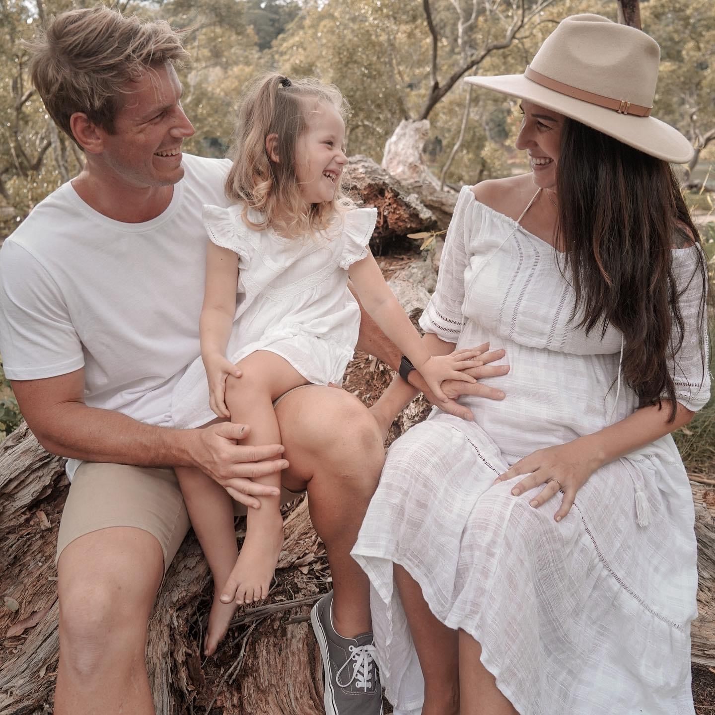 Family sharing a joyful moment while sitting on tree trunk in casual summer outfits.
