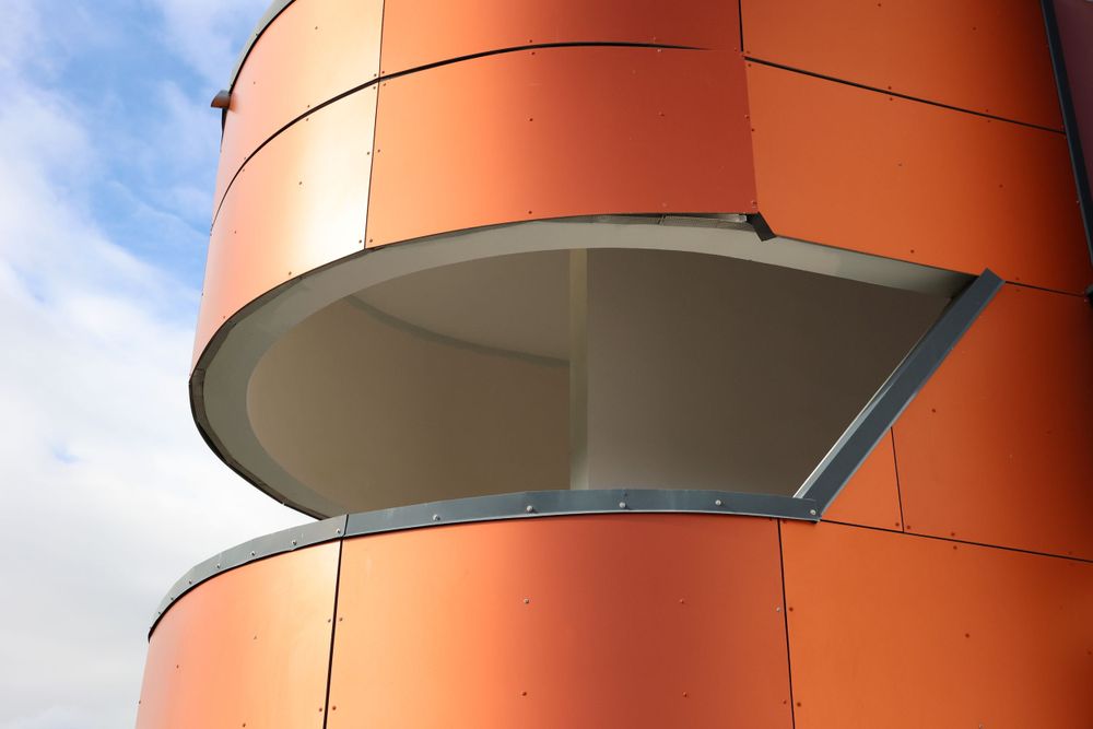 Abstract architectural detail of curved orange industrial structures against blue sky.