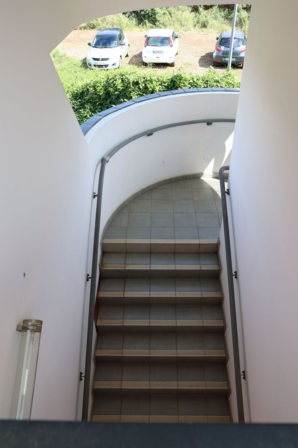 Curved stairwell entrance with white walls leading to outdoor parking area.