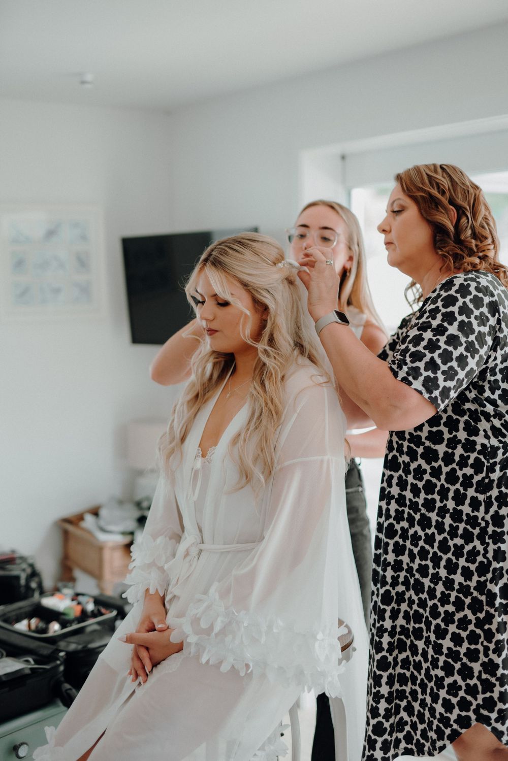 Bride getting ready with hair styling team in white preparation robe.